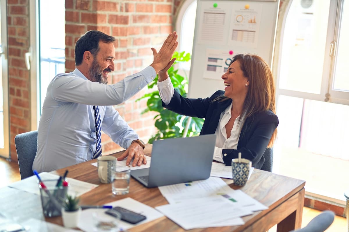 Two business colleagues celebrating with a high five at a desk